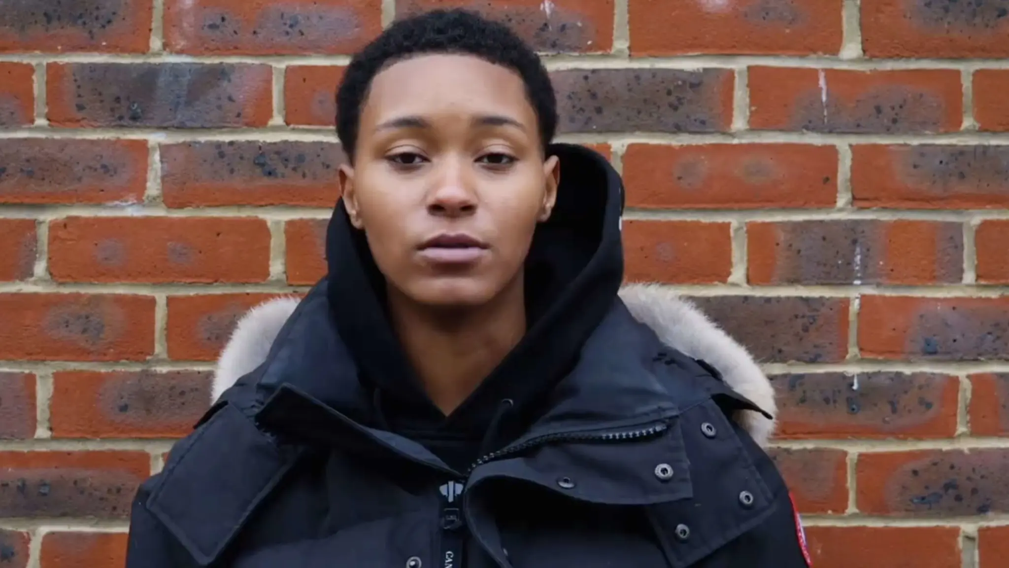 A screenshot from the video 'Jahiem's Justice Centre - why it matters to us' There is an image of a young black boy with short hair and a puffer jacket, he is looking into the camera standing in front of a brack wall.