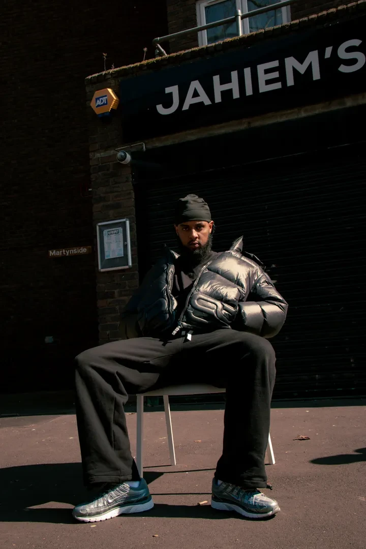 Young person sitting on a plastic chair with their hand in their pockets in front Jahiem's Justice Centre, looking at the camera with a serious expression.