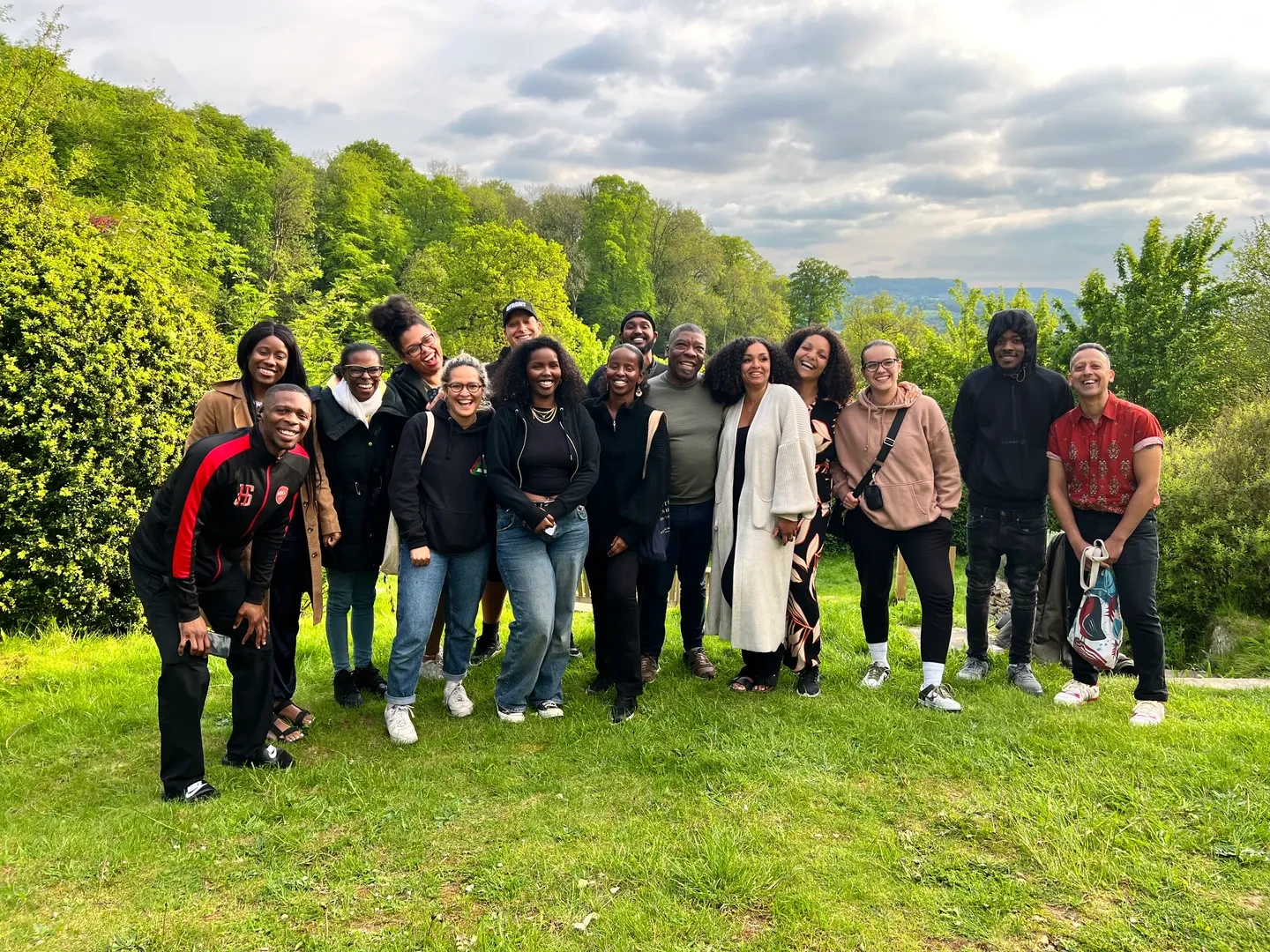 Large group of people in a natural environment, standing in front a forest looking at the camera with a smile.