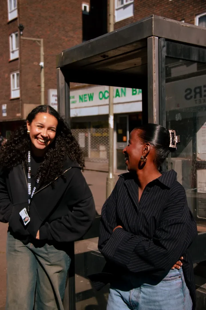 Two young people in an urban environment are looking at each other laughing. One of them is wearing a 4Front lanyard with a cardholder.
