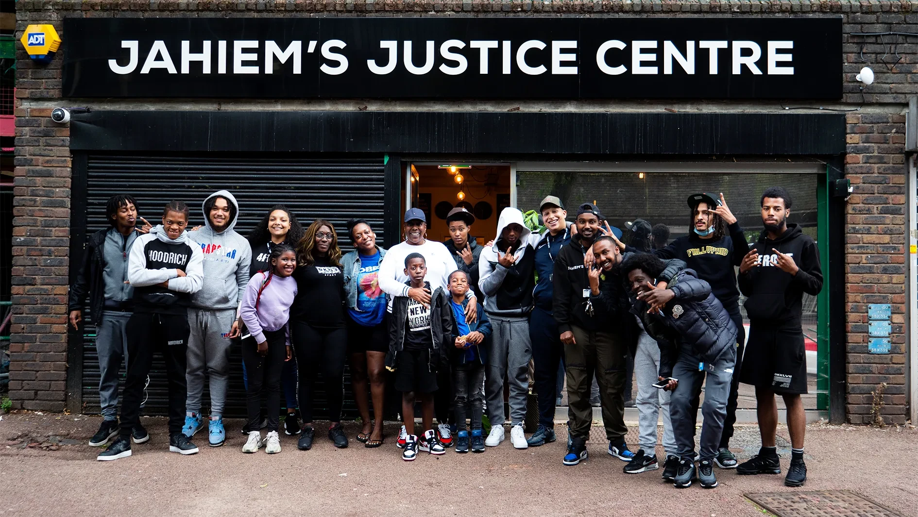 Large group of young people and children standing in front of Jahiem's Justice Centre, looking at the camera with a smile. Some of them are making various signs with their hands