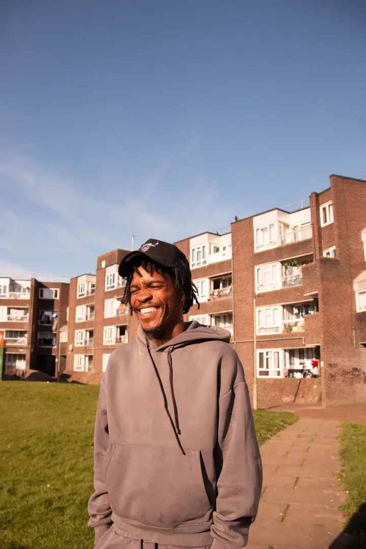 Young person standing in front of a building block with red brick walls, smiling.