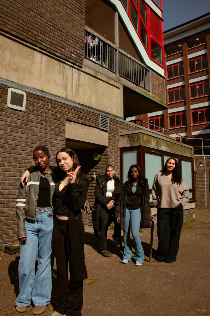 Small group of young people of diverse backgrounds standing in front of a building block, facing at the camera.