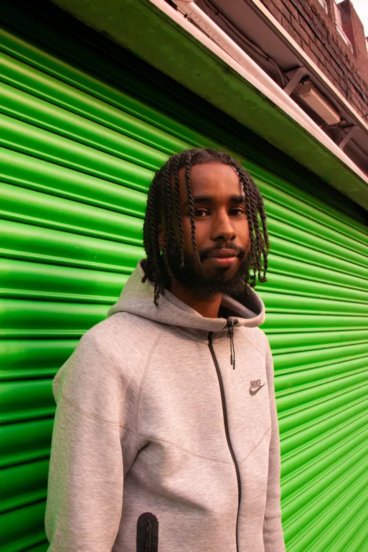 Young person with twist braids standing in front of Jahiem's Justice Centre's closed green shutter, looking at the camera with a friendly expression.