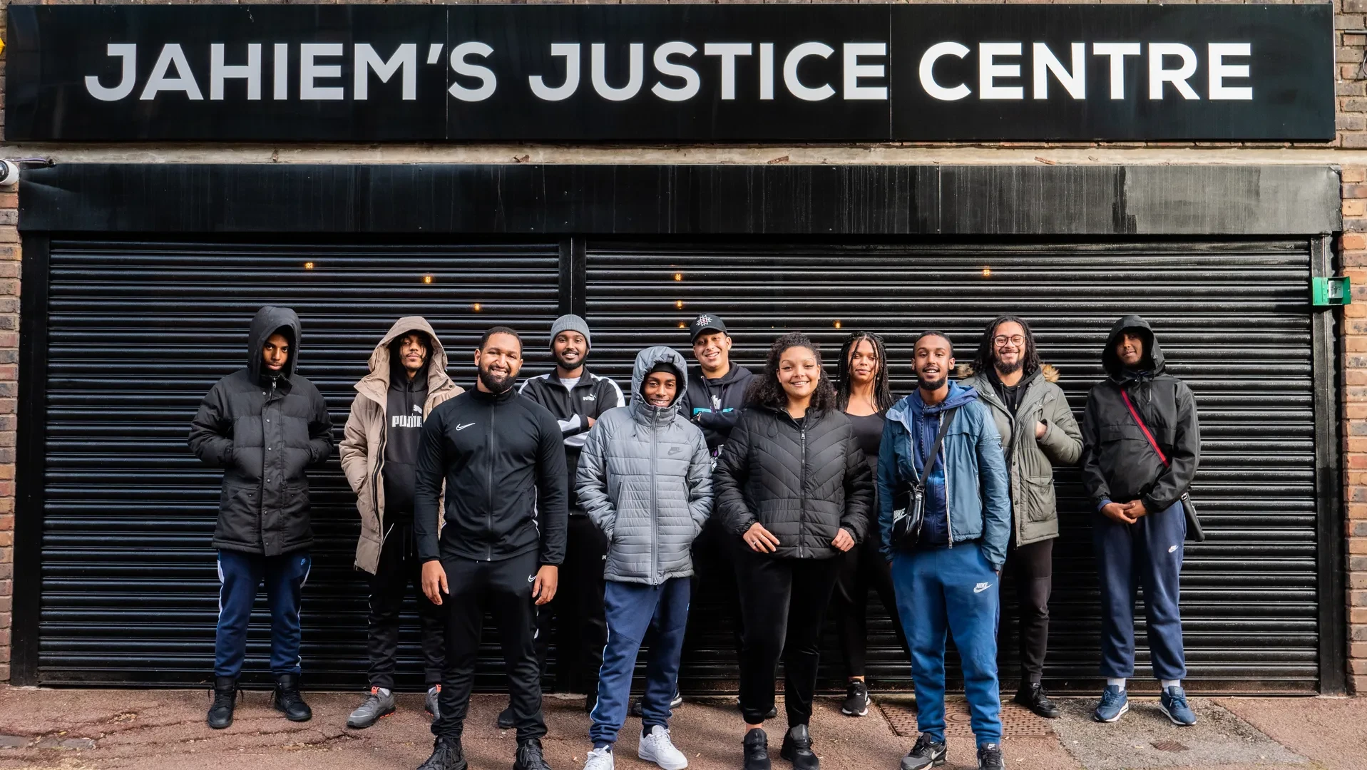 A group of smiling young black and brown people stand in front of Jahiem's Justice Centre in London.