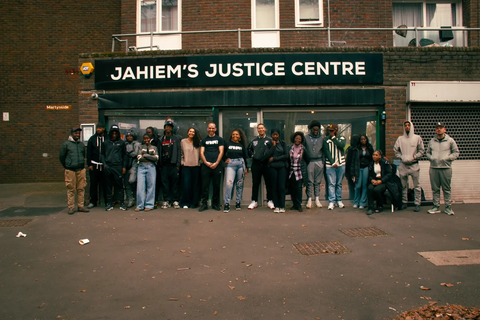 A group of smiling young black and brown people stand in front of Jahiem's Justice Centre in London.